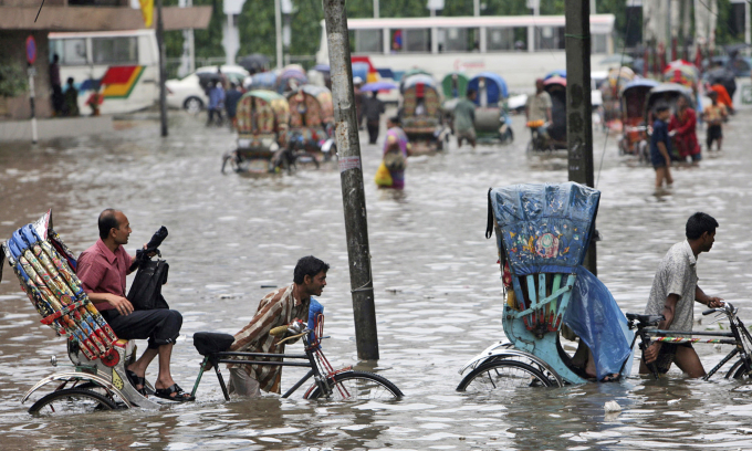 In this Tuesday, July 28, 2009 file photo, drivers pull their rickshaws carrying passengers through a flooded street in Dhaka, Bangladesh. (AP Photo/Pavel Rahman, File)